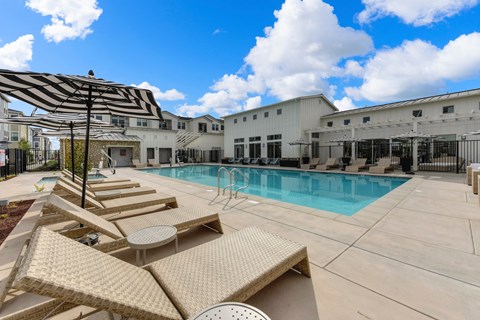 Outdoor pool area with tan colored lounge seating and black & white pool-side umbrellas.